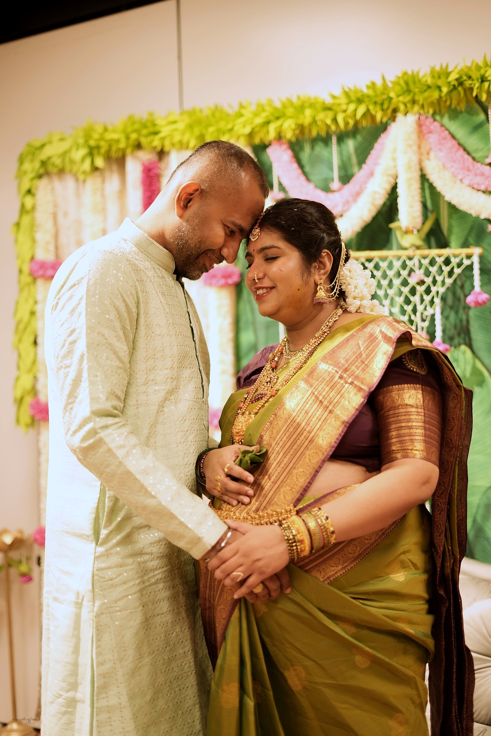 Couple embracing forehead to forehead at a baby shower, bride in traditional gold jewelry