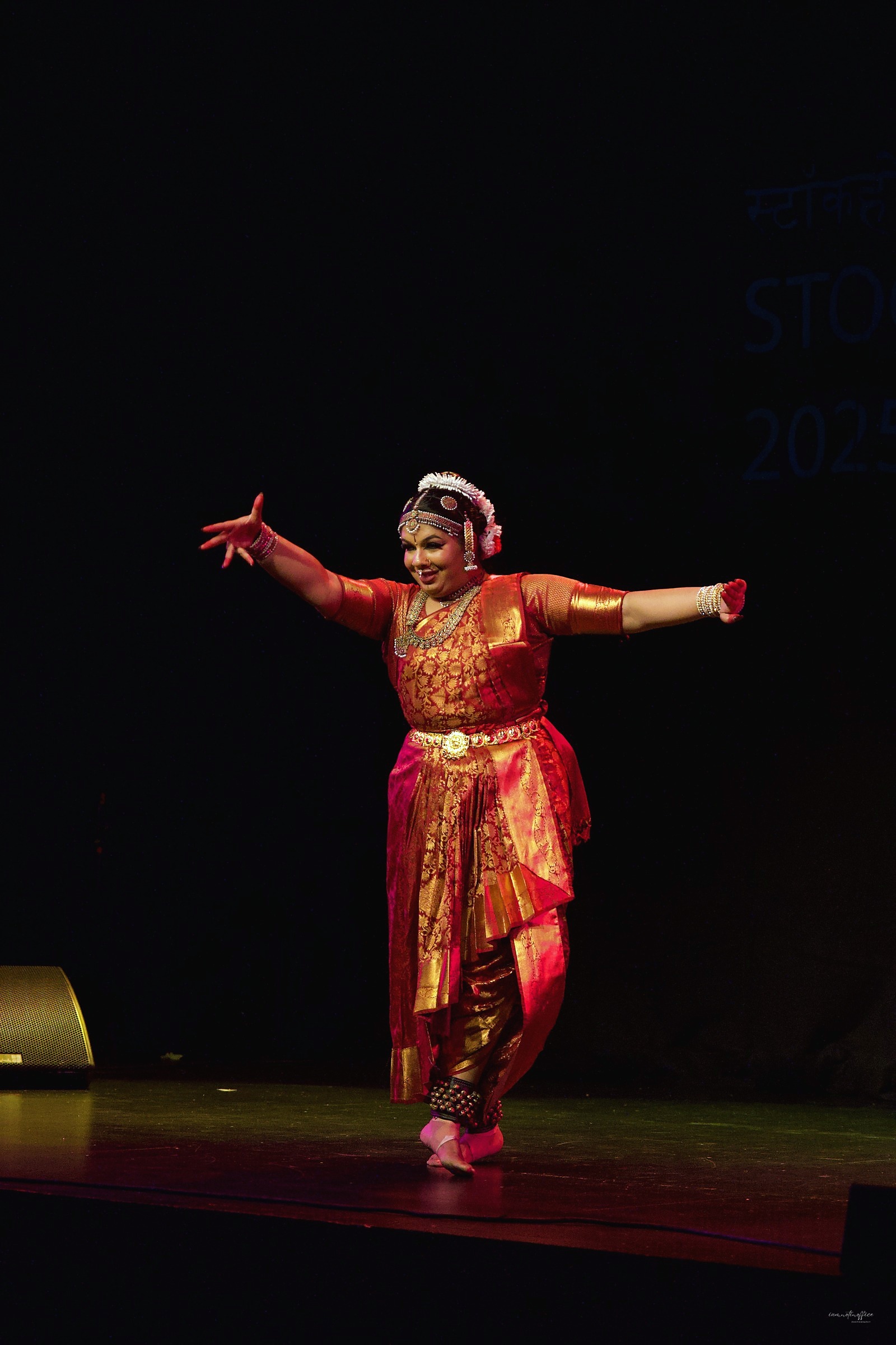 Classical Indian dancer mid-performance on a dark stage, arms extended