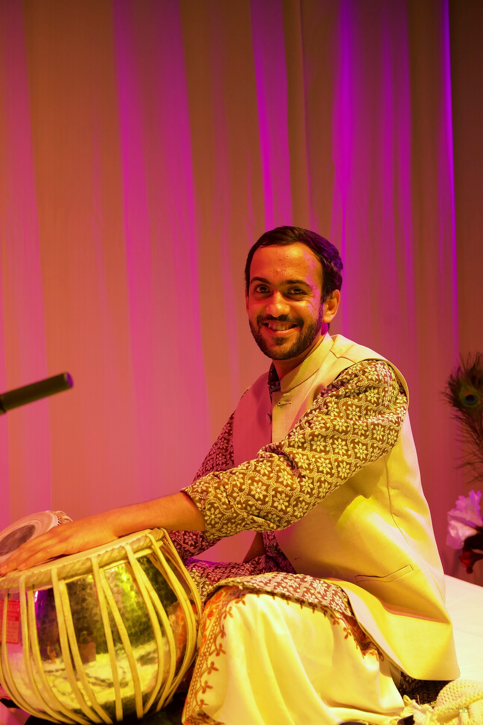 Tabla player smiling at the camera under pink stage light