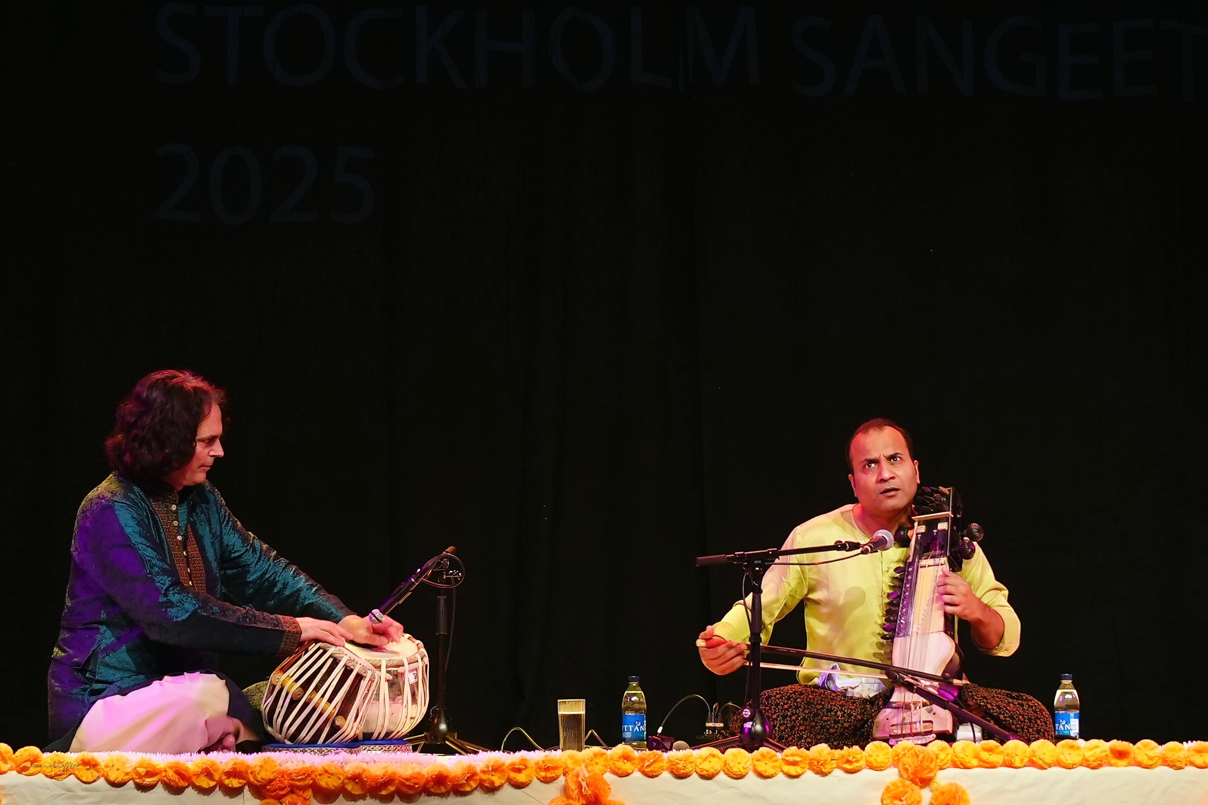 Two musicians performing together on stage, tabla and sarangi