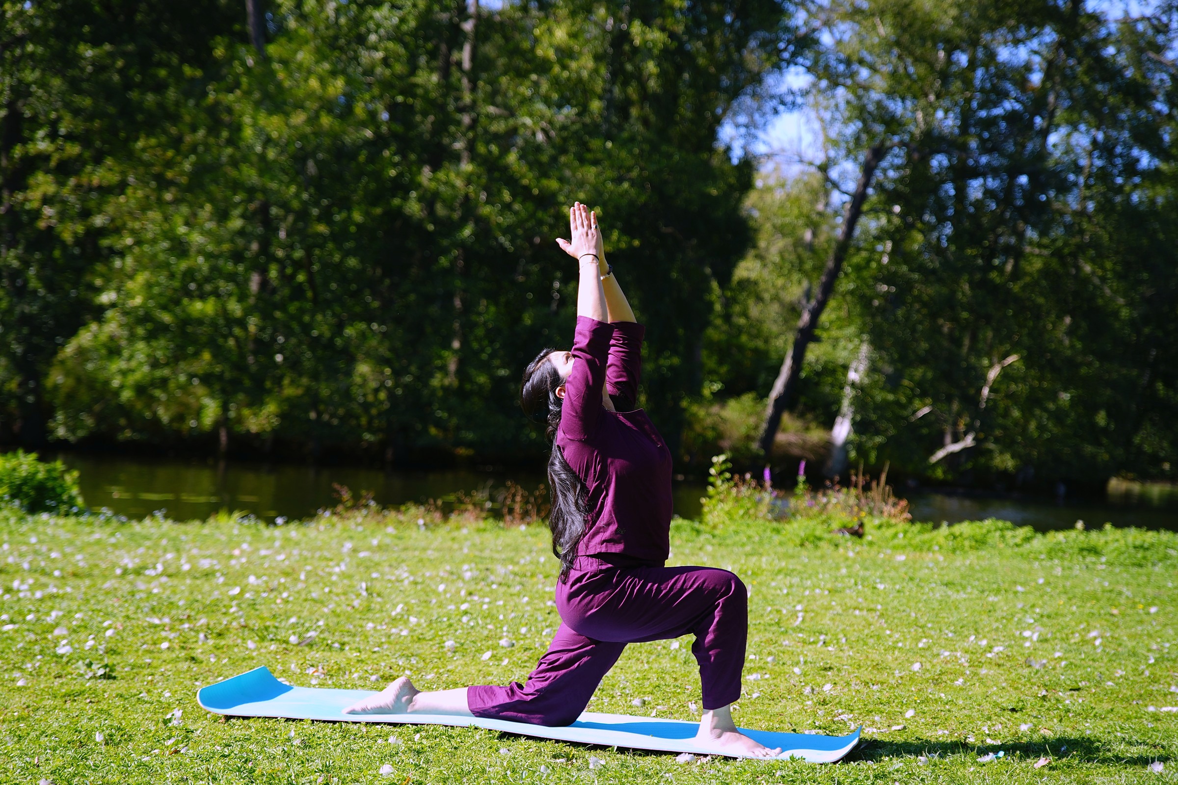 Woman in a crescent lunge yoga pose on a mat by a lake