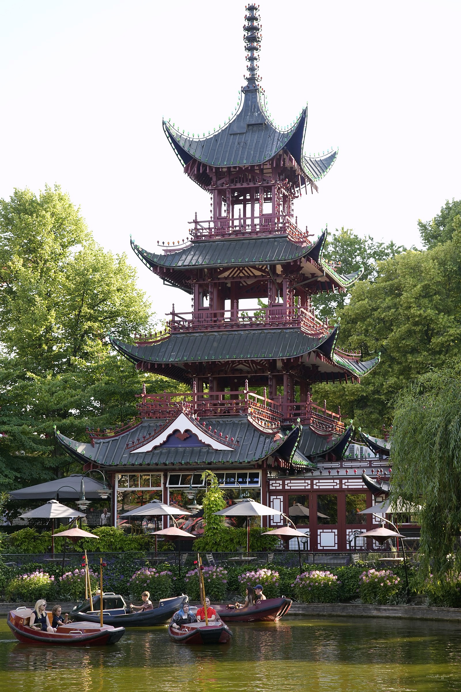 A multi-tiered Chinese-style pagoda beside a lake with pedal boats, framed by willow trees