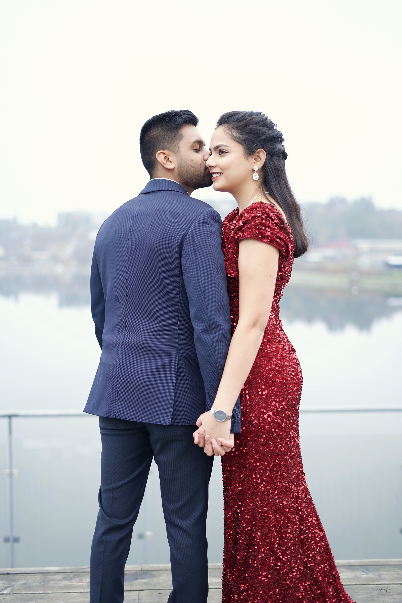 Couple embracing on a misty waterfront, groom kissing bride's cheek