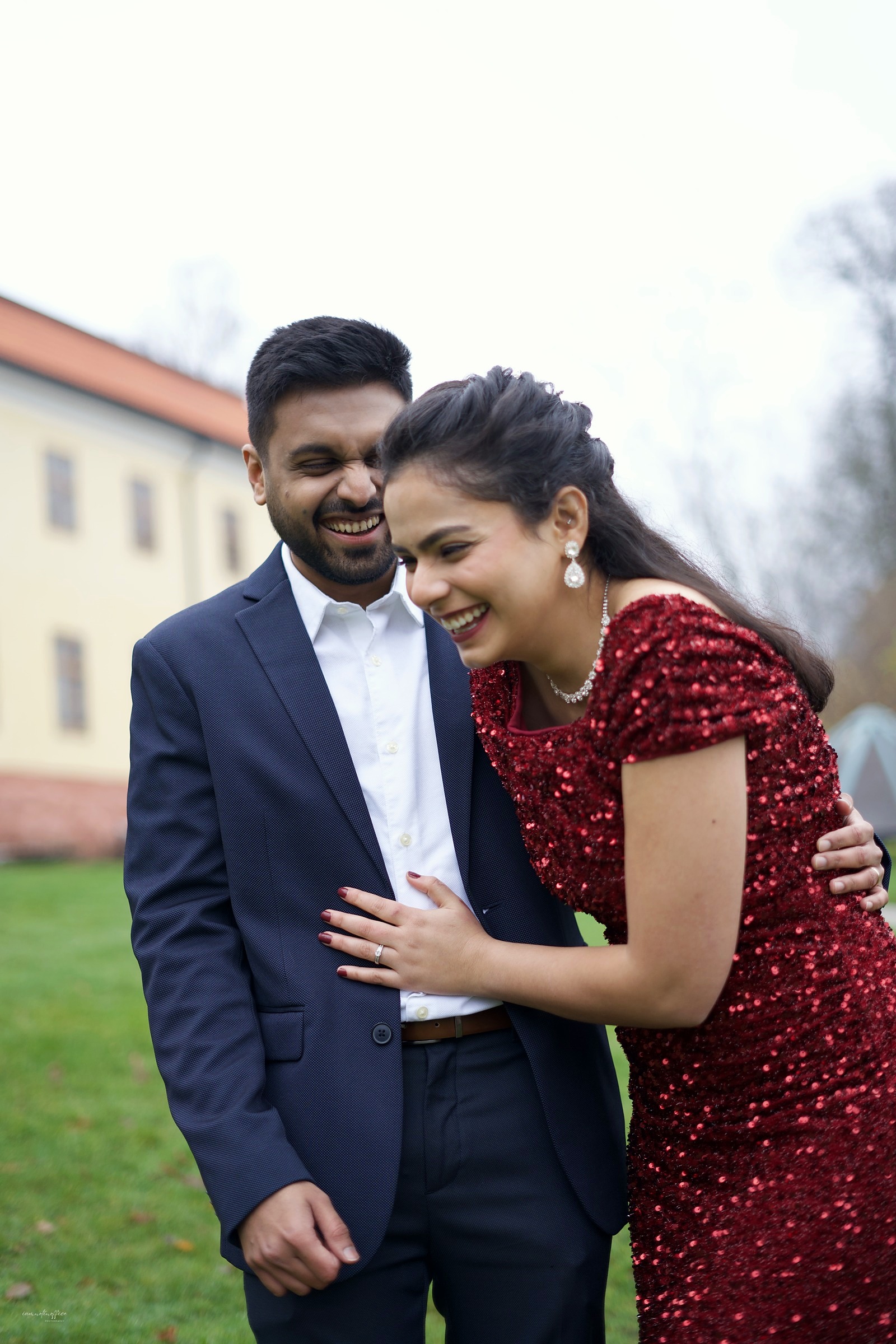 Couple laughing forehead to forehead on a palace lawn